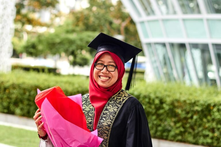 A proud female graduate in hijab with flowers celebrates her achievement outdoors.