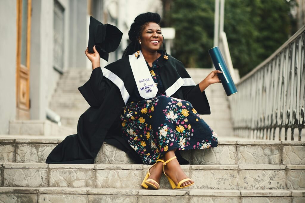 Woman joyfully celebrates graduation sitting on stairs with diploma and cap.